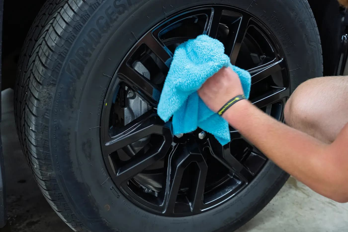 A detailer wiping down a black alloy wheel with a microfiber towel.