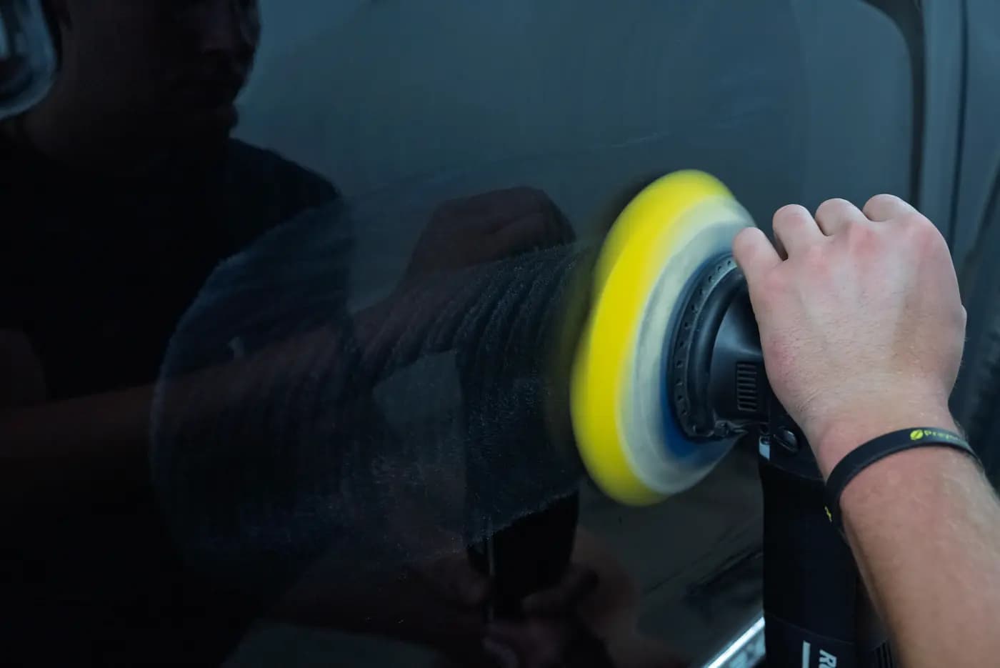 A detailer buffing a black body panel with a dual-action polisher.