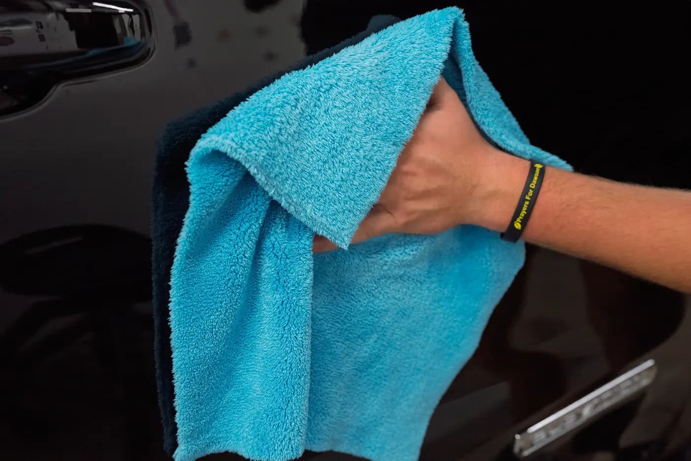 A detailer hand-drying a black door panel with a microfiber towel.